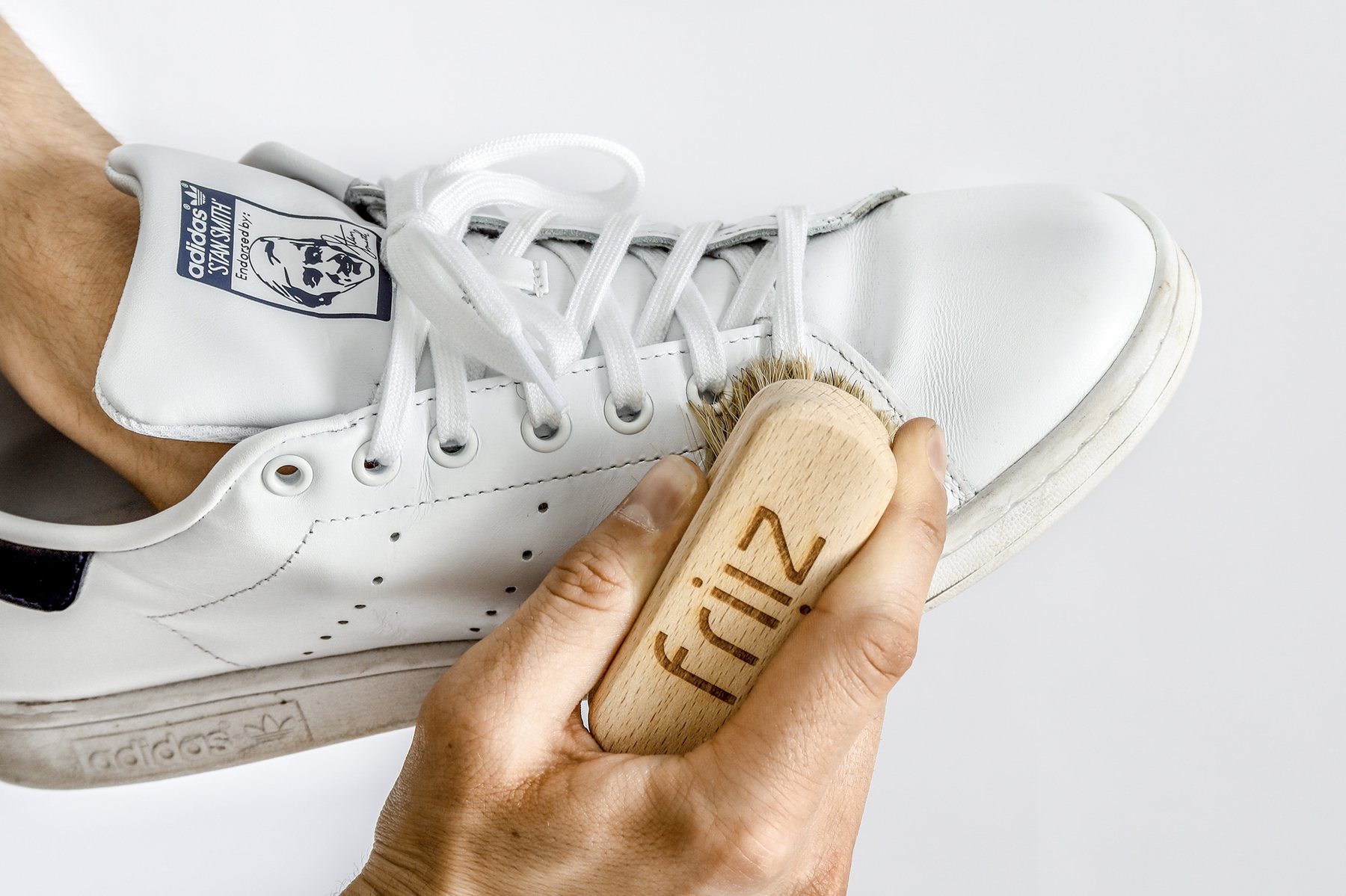 Makroaufnahme einer Schuhbürste beim Reinigen eines weißen Sneakers